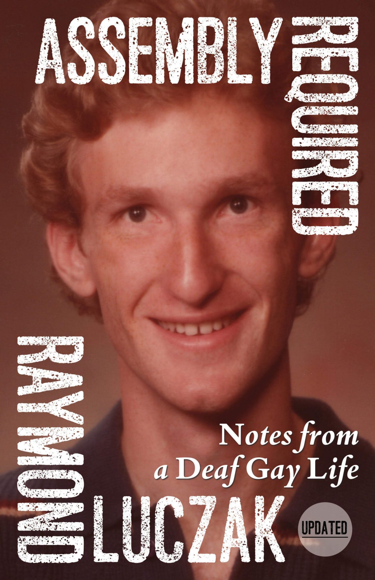 The mostly rust-colored cover shows the author's high school senior picture: He is clean-shaven, smiling with long hair swept to the side; his freckles have been airbrushed out. The title, subtitle, and author's name are arranged somewhat like a picture frame atop the picture: ASSEMBLY REQUIRED | Notes from a Deaf Gay Life (Updated) | RAYMOND LUCZAK.